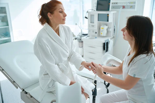 女医生牵着穿着长袍的病人的手 她们坐在妇科医生的椅子上 接受体外受精手术 — 图库照片