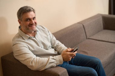 Rahat koltukta rahatlarken ve kameraya bakarken erkeğin cep telefonuna yan bakış