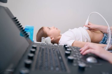 Küçük kız ultrason odasındaki tıbbi kanepede yatıyor. Doktor iç organların ultrasonunu yapıyor.