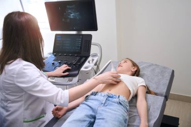Kadın doktor, küçük bir kızın iç organlarının ultrasonunu yapar. Teşhis uzmanı monitöre bakar.