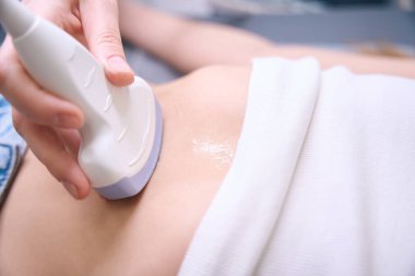 Teşhis uzmanı iç organların ultrasonu için modern ekipman kullanıyor. Hasta tıbbi bir kanepede yatıyor.