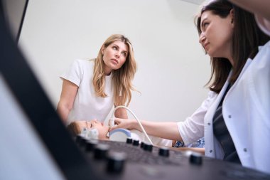 Anne ve kızı ultrason odasında tiroid bezi ultrasonu için, doktor cihazın monitörüne bakar.