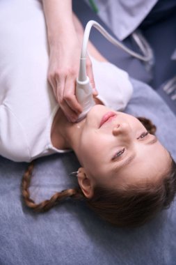 Tiroid bezinin ultrasonu için ultrason odasında örgü saçlı bir kız var. Doktor modern ekipman kullanıyor.