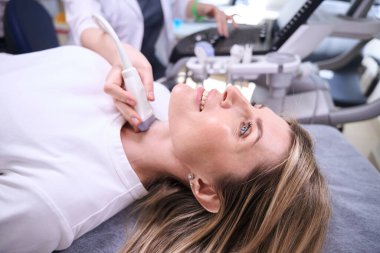Tiroid bezinin ultrasonu için klinikte hoş bir bayan var. Teşhisçi modern ekipman kullanıyor.