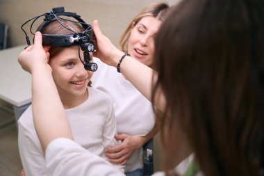 Bir otolarolog ile klinikteki küçük hasta, bir kız annesinin kucağına oturuyor.