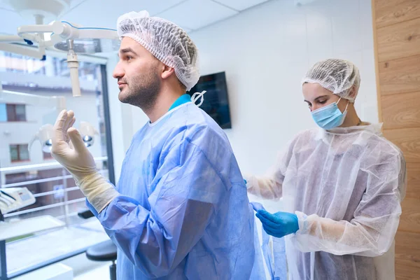 Hemşire Doktora Tek Kullanımlık Steril Bir Elbise Giydiriyor Ekip Ameliyata — Stok fotoğraf