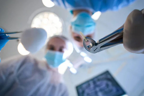 特殊部隊と手術室で彼の手に抽出された歯を持つ外科医 女性のアシスタントは彼を助ける — ストック写真