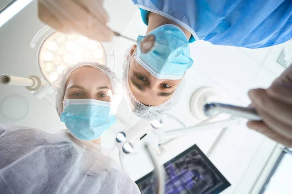 手術室の職場で歯科用鏡を手に外科医 女性のアシスタントは彼を助けます — ストック写真