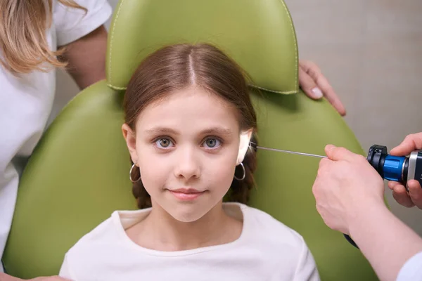医生对孩子们的耳朵进行了检查 这位漂亮的女孩正坐在一张绿色扶手椅上与一位耳鼻喉科医生约会 — 图库照片