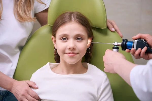 在与一位耳鼻喉科医生的约会中 一个沉着的女孩坐在一张绿色扶手椅上 医生检查孩子的耳朵 — 图库照片