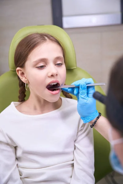 医学专家戴着防护手套检查孩子的喉咙 女孩坐在一张特殊的绿色椅子上 — 图库照片