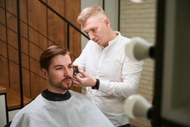 Kafkasyalı berber içeride saç kesen müşterisinin saçını kesiyor.