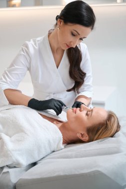 Genç bir kadın gençleştirici enjeksiyon uyguluyor. Uzman, ince bir iğne kullanıyor.