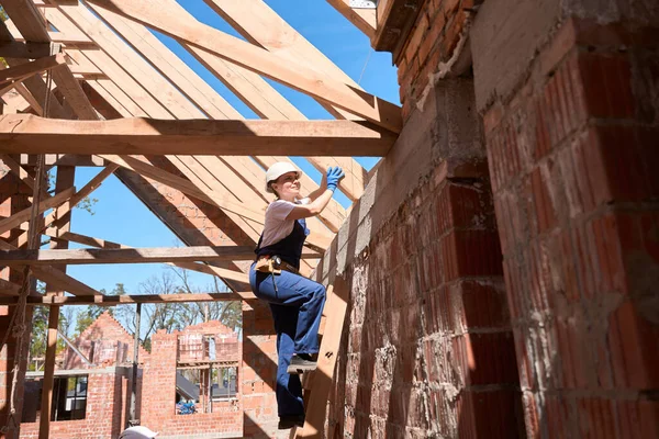 女性の一般請負業者は 天井構造の支持梁の強度を確認するために木製のはしごを登ると 工事現場を監督 — ストック写真