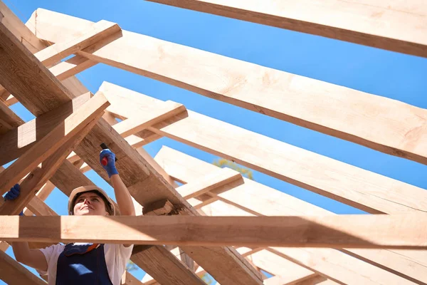 细心的女总承包人 戴着硬礼帽 把钉子钉在屋顶施工的木架上 在工地辛勤劳作 — 图库照片