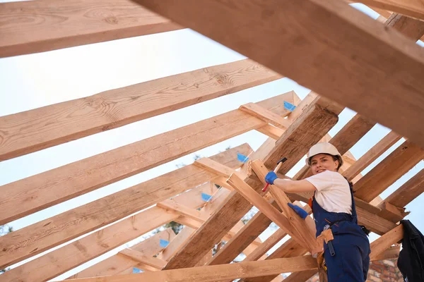 より良いと信頼性の高いヒッチングのための木造屋根の建設に硬さと均一なハンマー釘で笑顔の女性大工 建設現場で働く — ストック写真