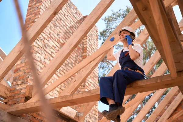 Radosna Kobieta Dekarz Siedzi Drewnianej Belce Konstrukcji Dachu Rozmawia Przez — Zdjęcie stockowe