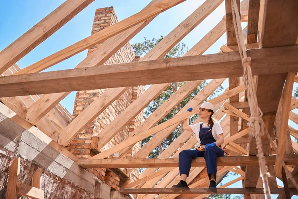 屋根枠の梁に座って建設現場を見て責任ある女性ゼネコン 定性的な仕事に満足 — ストック写真