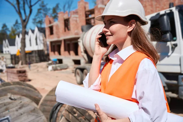 身穿硬帽和安全背心的合格女建筑师会说话电话 接受总承包商的指示 花时间在建筑工地 — 图库照片