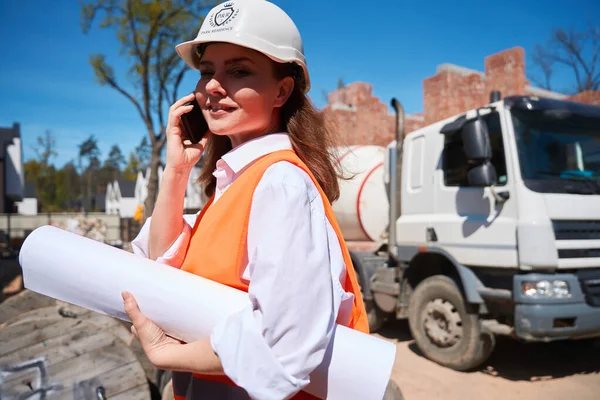 ハードハットの女性建設労働者が設計図を保持し 投資家や住宅開発業者と電話をかけ 指示を受ける — ストック写真