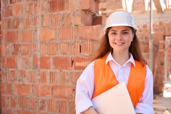 ハードハットとオレンジの安全ベストの正の女性建築家は ラップトップを保持し 建設現場で笑みを浮かべて 3Dビルディングモデル — ストック写真