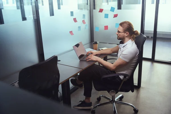 ガラスの男はノートパソコンのオフィスブロックで働いてるオフィスの椅子に座ってる — ストック写真