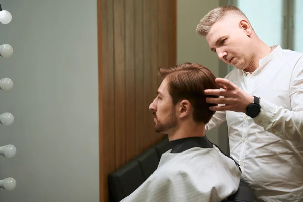 Pečlivý Holič Styling Vlasy Svého Klienta Který Nosí Stříhání Vlasy — Stock fotografie