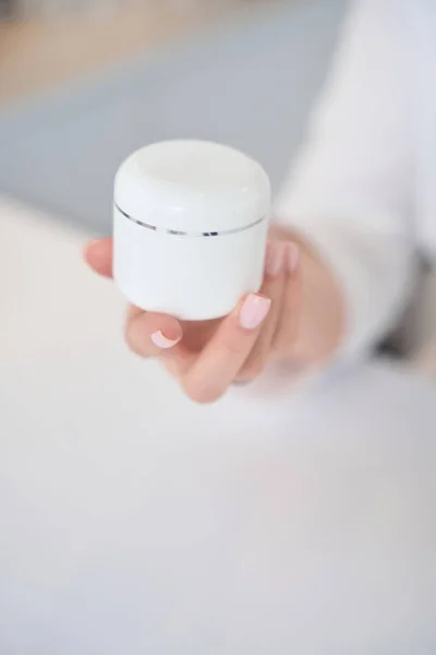 stock image Specialist cosmetologist demonstrates a white jar of anti-aging face cream, a woman has a neat manicure