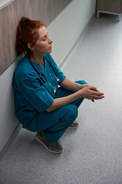 Utmattad Kvinnlig Läkare Som Sitter Nära Väggen Sjukhuskorridoren Efter Svårt — Stockfoto