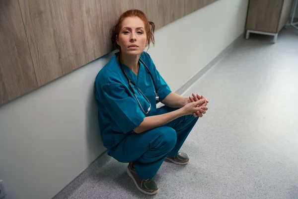 長い一日の後に廊下に一人で座って疲れ女性看護師クリニックで働く — ストック写真