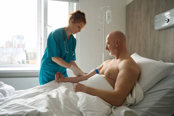 女医生用注射器从病人手臂静脉中提取血液样本 病人躺在病床上进行临床观察 — 图库照片
