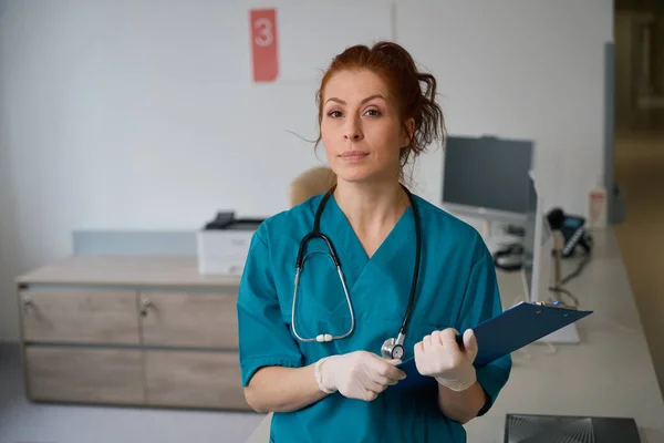 诊所办公室穿着制服和橡胶手套站在剪贴板上的成年女医生画像 — 图库照片