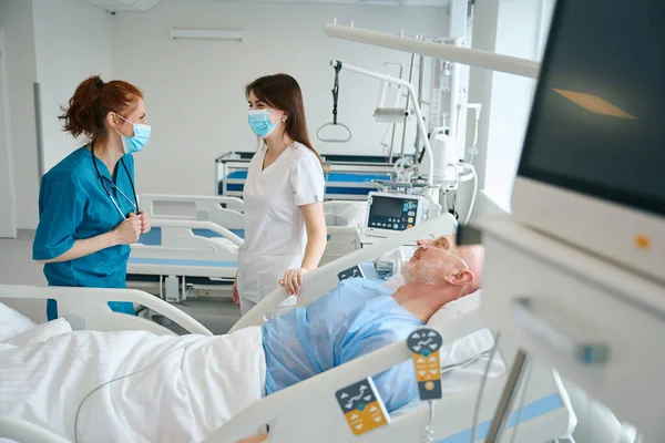 医生和女医生站在躺在急救室的患病男病人旁边 — 图库照片