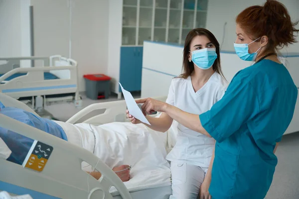 Assistentes Médicas Durante Dia Trabalho Visitam Paciente Deitado Cama Discutem — Fotografia de Stock