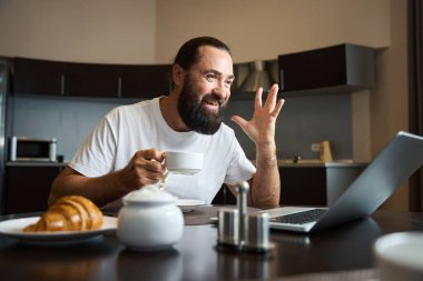 Adam kahve içiyor ve internetten duygusal olarak iletişim kuruyor. Mutfak alanında bir masada oturuyor.