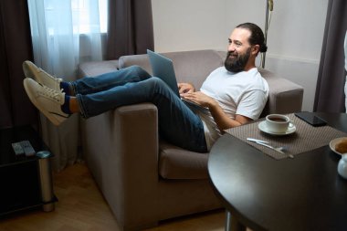 Rahat bir koltukta dizüstü bilgisayarlı bir otel müşterisi oturuyor. İnternetten iletişim kuruyor.