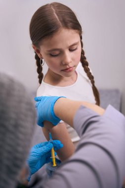 Enjeksiyon odasındaki güzel kız eline iğne yaptırıyor, doktor ince bir iğne kullanıyor.