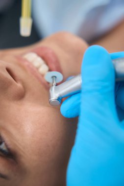 Kadın hastaya profesyonel diş temizliği yapmak için diş matkabı ve diş macunu kullanıyor. Hemşire tükürüğü özel vakum cihazıyla çıkarıyor.