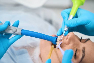 Doktor randevusundaki hasta diş hekiminin koltuğundadır, doktor iş için özel aletler kullanır.