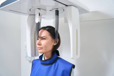 Esmer kadın röntgen odasında teşhis işleminde, koruyucu önlük de hastanın üzerinde.