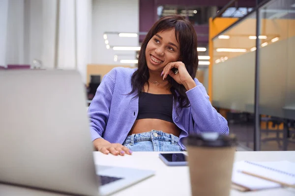 African American woman with braces smiling while working with notebook computer in modern office