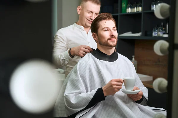 Cliente Masculino Confiante Bebendo Café Enquanto Cabeleireiro Servindo Barbearia Moderna — Fotografia de Stock