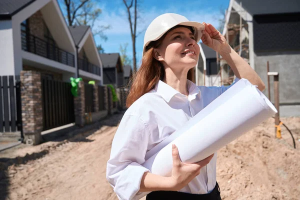 Positive woman landscape designer coming to construction site to examine it and draw exterior design plan, working with blueprints, legalizing construction