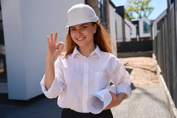 Wesoły Pewny Siebie Architekt Kobieta Planami Rękach Hardhat Pokazując Gest — Zdjęcie stockowe