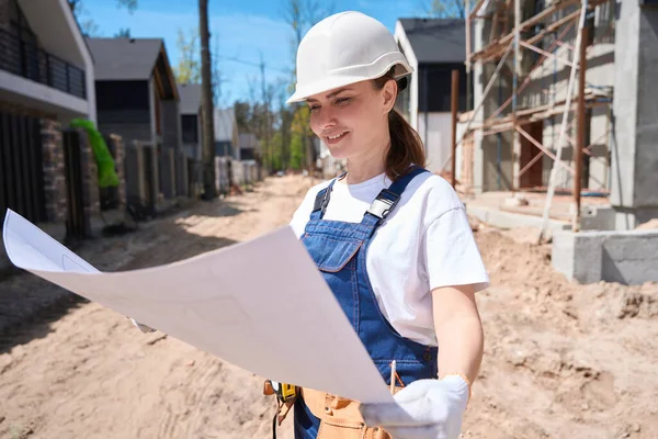 身穿硬帽的女土木工程师面带微笑 纵观整个建筑蓝图 到达工地开始施工 — 图库照片