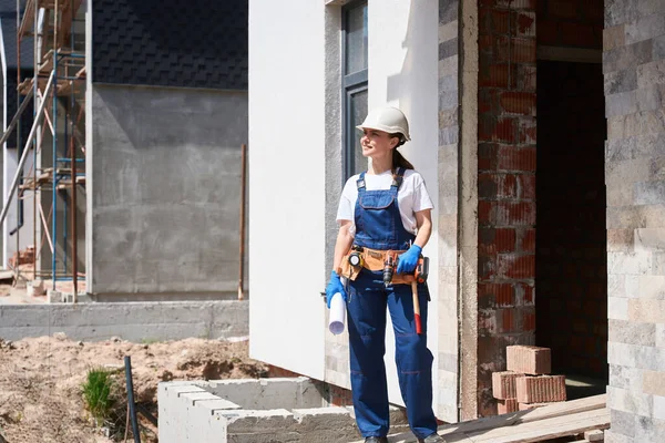 微笑的女建筑工程师 带着工具带站在建筑入口下的房子里 准备开始内部工作 并保持设计计划 — 图库照片
