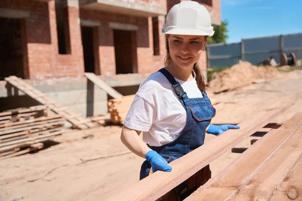 笑顔の女性ハンディマンは 建設現場で木製のビームをアンロードしてソートするのを手伝い 材料を保持し 2階の屋根 — ストック写真