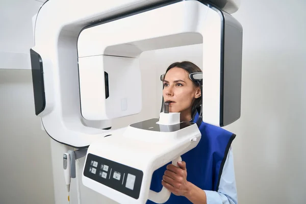 Brunette patient in a protective apron is undergoing a 3D scanning procedure using modern equipment