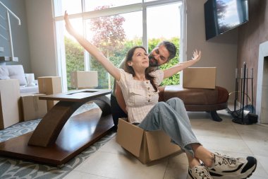 Çekici kadın kutunun üzerinde oturuyor ve kollarını yana açıyor. Erkeği de içeride oturuyor.