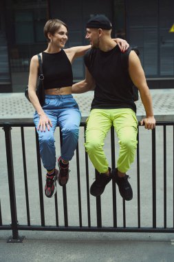 Hoş kadın ve erkek, günlük giysiler içinde parmaklıkların üzerinde oturup birbirlerine sevgi gösteriyorlar.